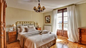 Une chambre à coucher avec un lit en bois, des tables de chevet, un lustre, une fenêtre avec des rideaux et un tableau au mur.