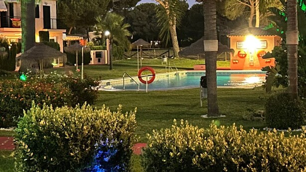 A pool area with a red circular sign, palm trees, and a building with a lit-up facade. - Holiday Home 'Islantilla' with Shared Pool, Private Terrace and Wi-Fi (Islantilla)