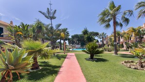 A pathway leading to a pool area surrounded by palm trees and well-maintained grass. - Holiday Home 'Islantilla' with Shared Pool, Private Terrace and Wi-Fi (Islantilla)