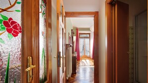 A hallway with wooden doors, a tiled floor, and a view into a room with a window and curtains.