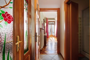 Ein Flur mit Holztüren, gefliestem Boden und Blick in einen Raum mit Fenster und Vorhängen.