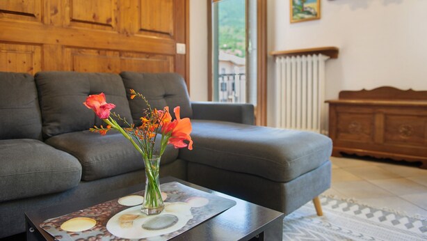 A living room with a grey sofa, a wooden cabinet, and a vase with flowers on a table.