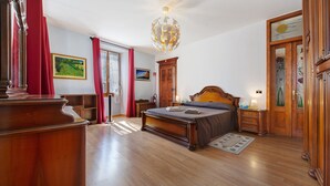 A bedroom with a wooden bed, a nightstand, a dresser, a chandelier, and a door with a glass panel.