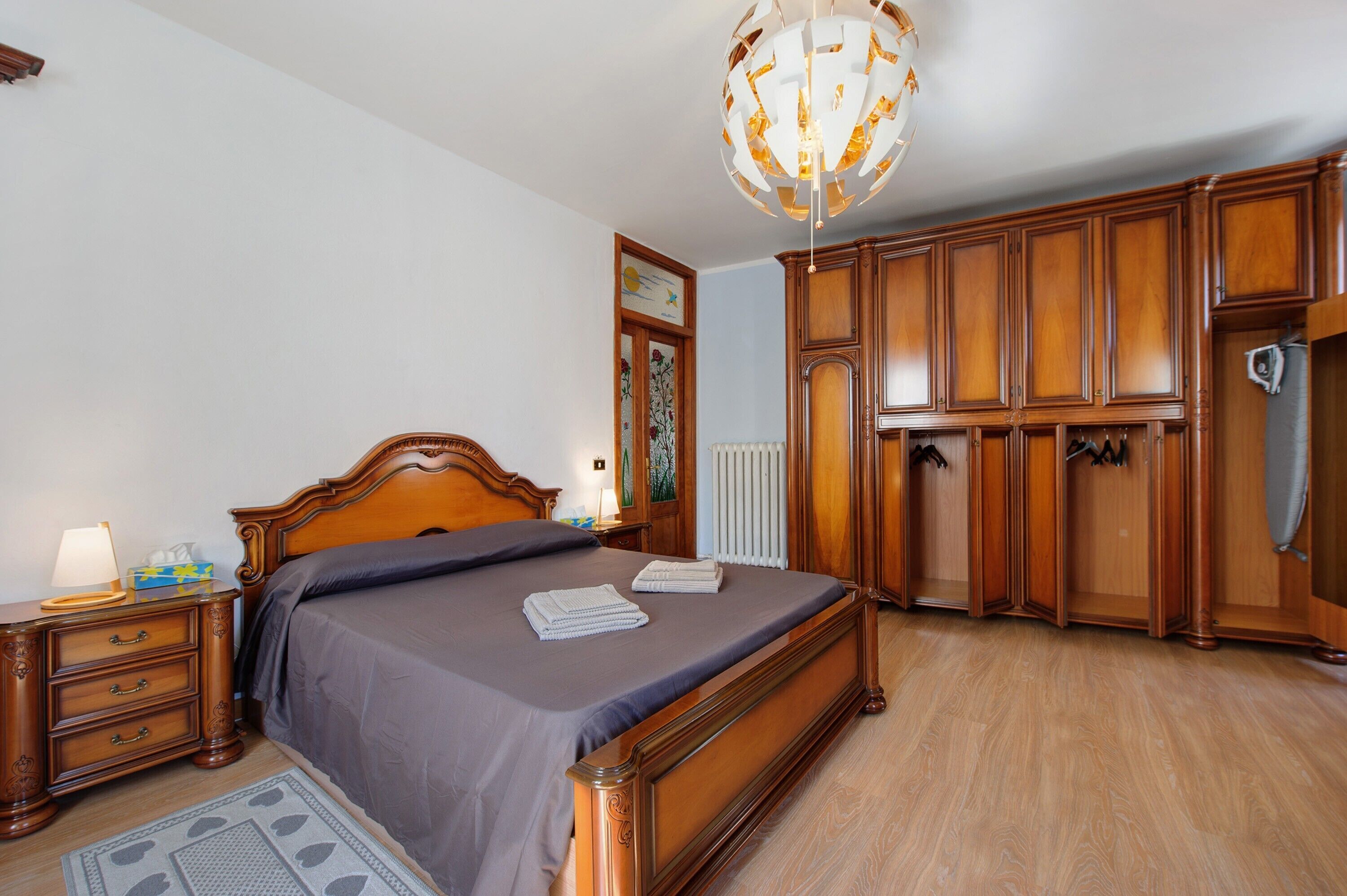 Een slaapkamer met een houten bed, een nachtkastje, een kaptafel en een kroonluchter.