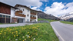 A modern building with a wooden balcony, a gravel driveway, and a road curving to the right. - Apartment "Edelweiss" with mountain view, private terrace and Wi-Fi (Curon Venosta)