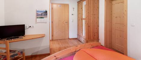 A bedroom with a bed, a TV on a wooden stand, wooden doors, and a small wooden cabinet.