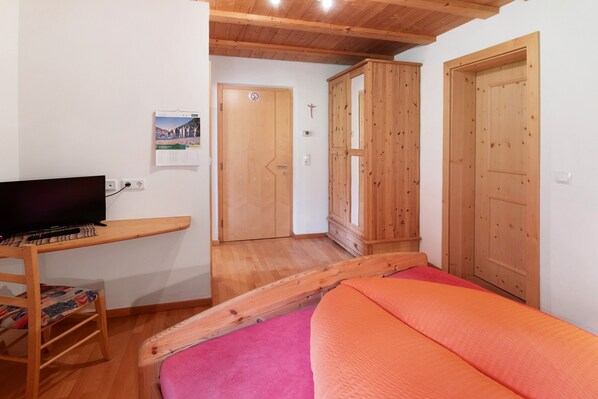 A bedroom with a bed, a TV on a wooden stand, wooden doors, and a small wooden cabinet.