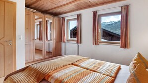 A bedroom with a bed, wooden wardrobe, and windows with curtains. - Apartment "Edelweiss" with mountain view, private terrace and Wi-Fi (Curon Venosta)