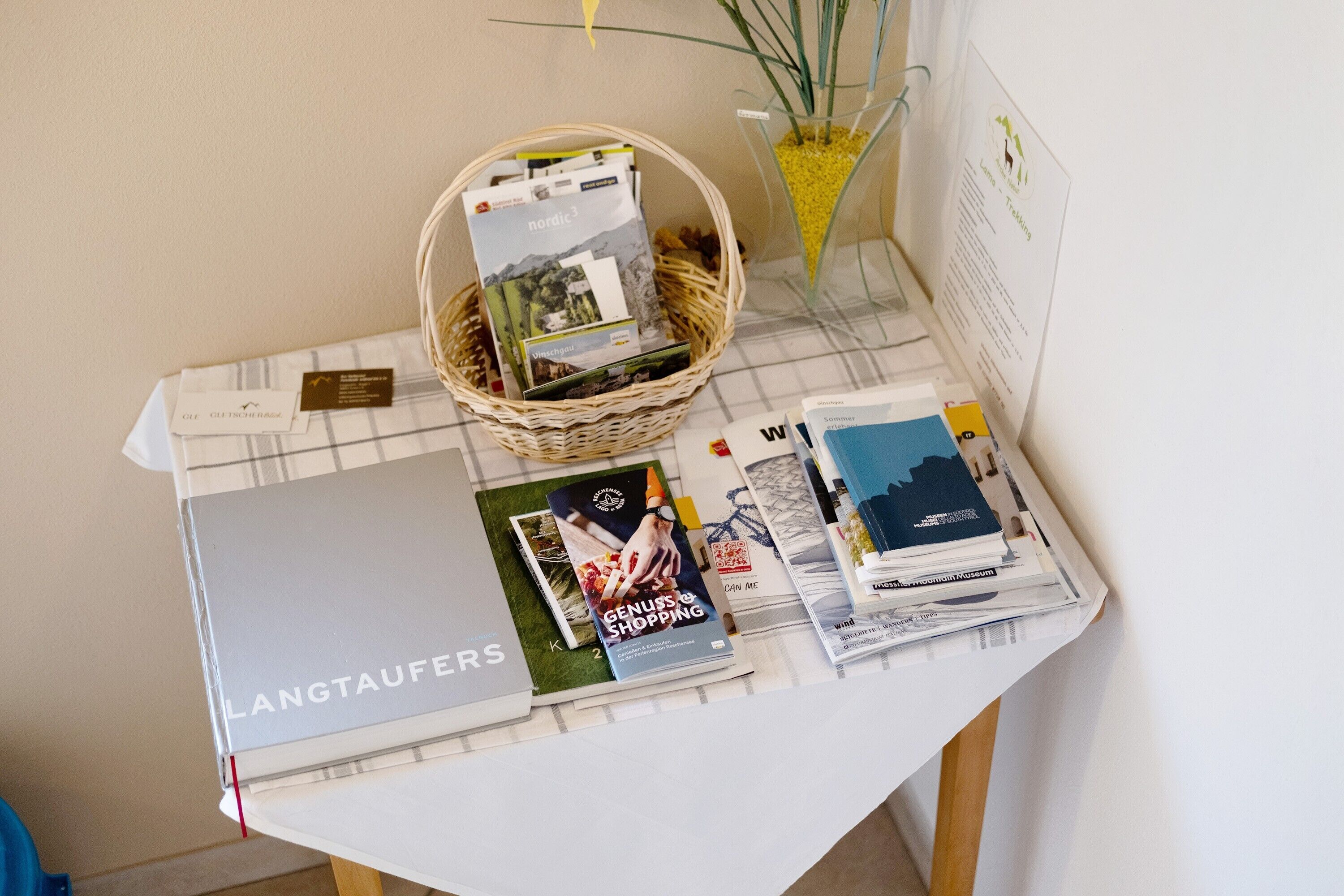 Ein Tisch mit einem Magazinnetz, einem Buch mit dem Titel 'GENUINE SHOPPING' und einer 'LANGTAUFERS'-Box.