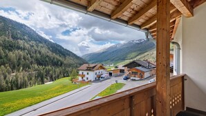 Vista de la montaña desde un balcón de madera, con un camino que lleva a un conjunto de edificios.