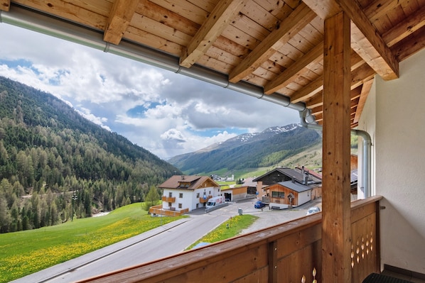A mountain view from a wooden balcony with a road leading to a cluster of buildings.