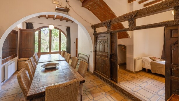 A dining area with a long wooden table, wicker chairs, and a large arched window. - Villa 'Casa Argentera' with Mountain View, Private Pool and Wi-Fi (L'Argentera)