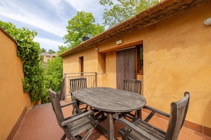 Une terrasse avec une table ronde en bois et des chaises, un sol carrelé et un mur jaune avec une fenêtre.