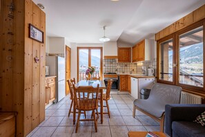 A kitchen with wooden cabinets, a dining table with chairs, a sofa, and a view of mountains through large windows.