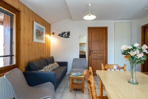A cozy living room with a sofa, a dining table, and a vase of flowers. - Apartment 'La Favière' with Mountain View, Balcony and Wi-Fi (Val-Cenis)
