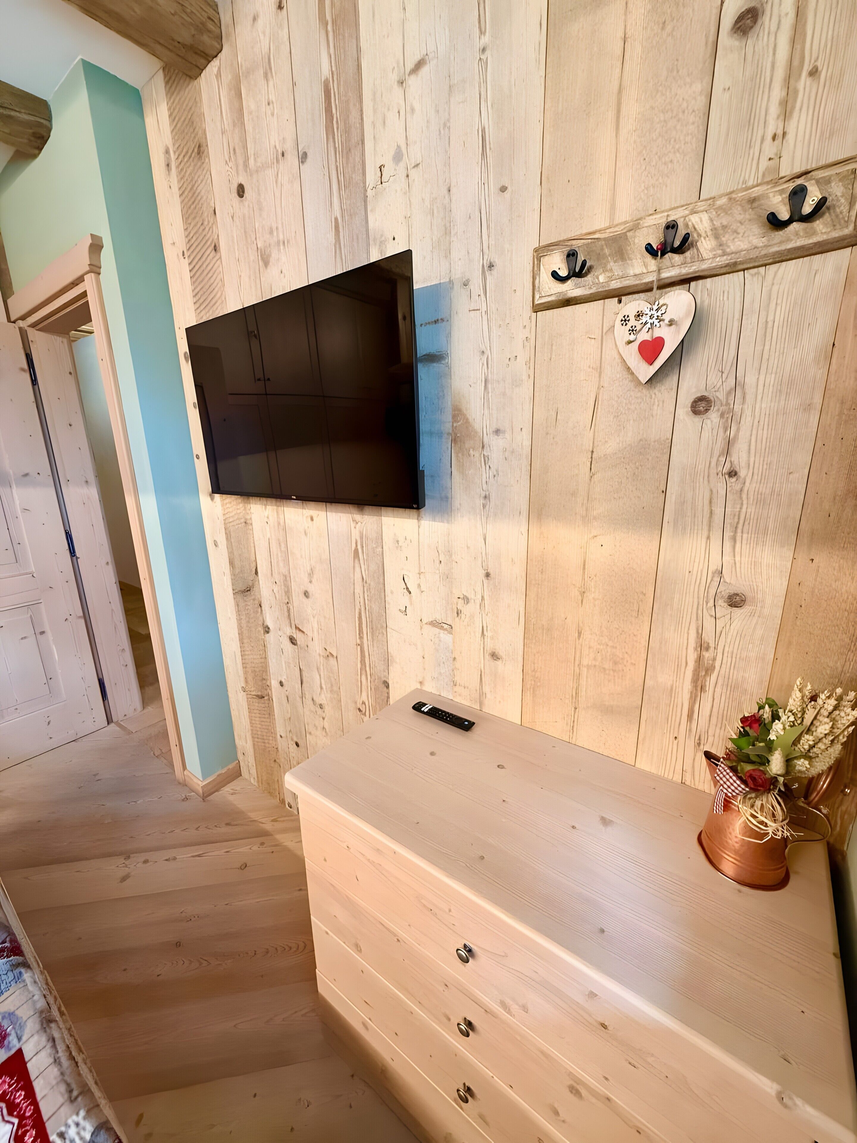 A room with a wooden wall, a mounted TV, a wooden dresser, and a heart-shaped decoration with a remote control on top.