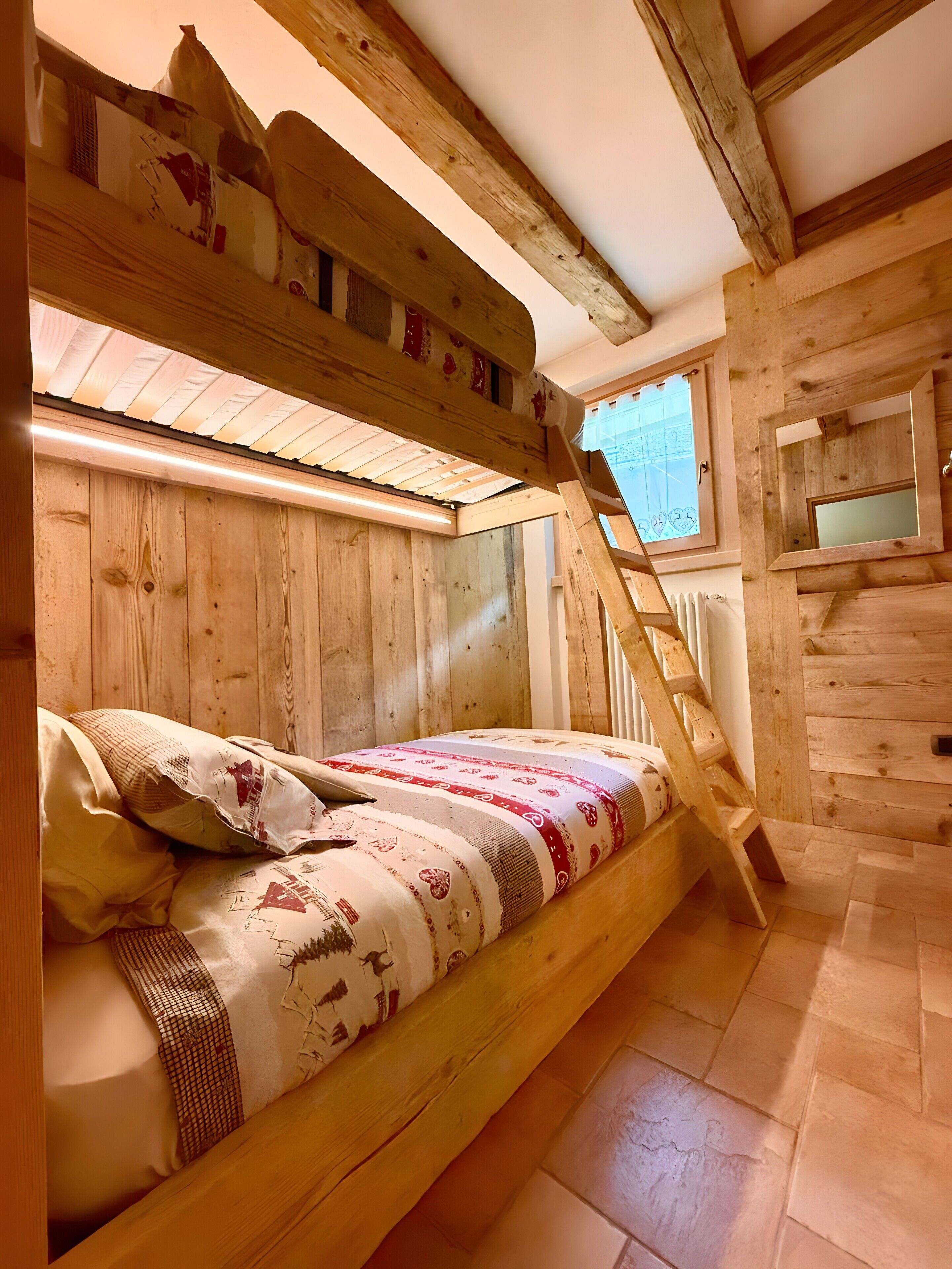 Un lit superposé avec une tête de lit en bois, une fenêtre donnant sur un beau paysage et un petit miroir accroché au mur.