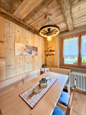 Interior de madera con una mesa larga, bancos, un ventilador de techo, un radiador y una ventana con vistas.
