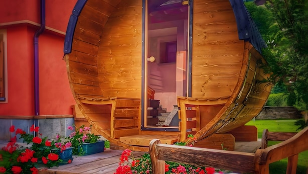 Una estructura en forma de barril de madera con una puerta, escalones que llevan a ella y un pequeño espacio al aire libre con bancos.