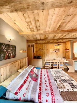 Una habitación acogedora de estilo cabaña, con techo de madera, una cama con ropa de cama estampada, un comedor con mesa y sillas, y una cocina con microondas y armarios.