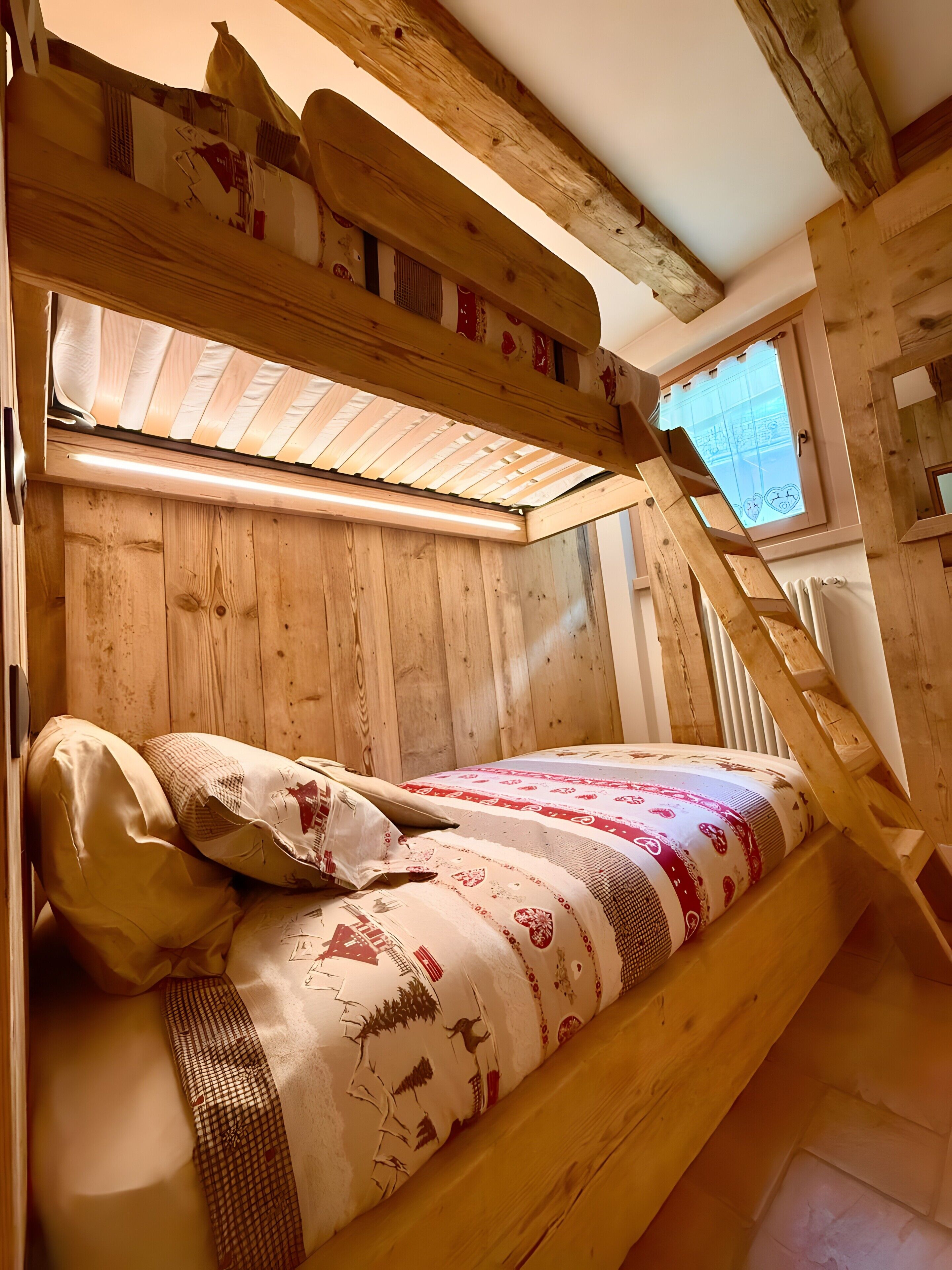 A wooden bunk bed with a slanted ceiling, a window with a view, and a patterned bedspread.