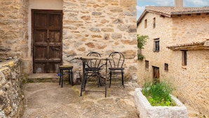 A stone building with a wooden door, a small outdoor seating area with metal chairs, and a narrow pathway. - Farmhouse 'Moli D'en Pi' with Mountain View, Shared Terrace and Private Garden (Morella)