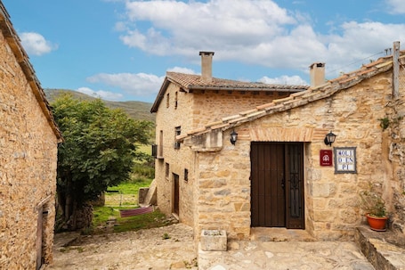 A stone building with a dark wooden door, a small garden, and a sign indicating a restaurant.