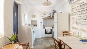 A compact kitchen with a stone floor, white walls, a blue door, and a dining area with a table and chairs.