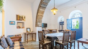 A cozy room with a stone arch, a dining table with chairs, a sofa with patterned cushions, a television, and a bookshelf.