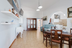 A dining area with a wooden table and chairs, a blue sofa, and a kitchen in the background.