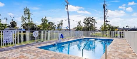 A rectangular swimming pool with a tiled deck, surrounded by a white fence and a lifeguard chair.