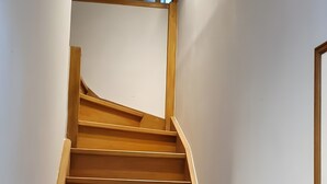 Un escalier en bois avec une rampe, menant à un palier dont le mur est décoré de rayures bleues et blanches.