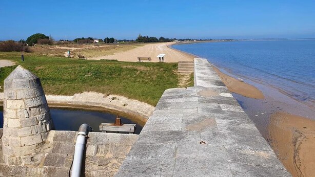 Une vue sur la côte, avec une structure en pierre, une plage de sable et un ciel bleu dégagé.