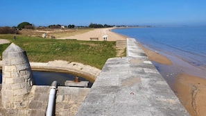 Une vue sur la côte, avec une structure en pierre, une plage de sable et un ciel bleu dégagé.