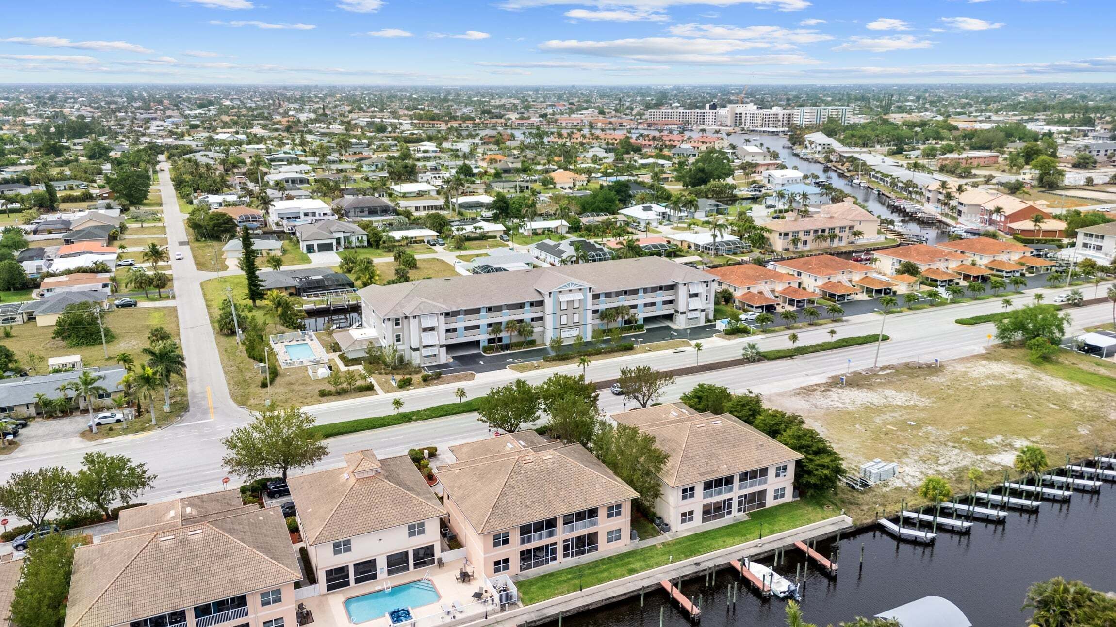 A residential area with a large building featuring a swimming pool, a marina with boats, and a clear view of the surrounding neighborhood.