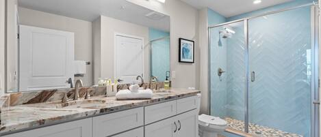 A modern bathroom with a marble countertop, a glass shower enclosure, and a large mirror.
