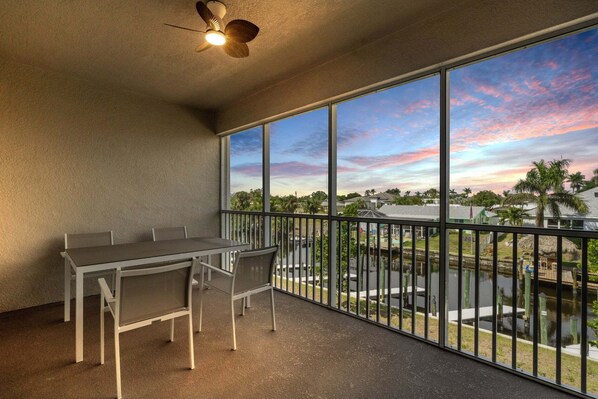 Un balcon avec une table et des chaises, un ventilateur de plafond et une vue sur une étendue d’eau et des bâtiments.