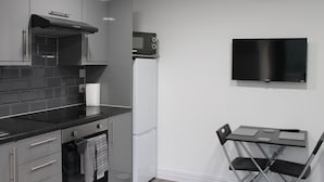 A compact kitchen with grey cabinets, a black countertop, a microwave, a white refrigerator, and a foldable table with chairs. - 6BV Apartment - Bevois Valley (Southampton)