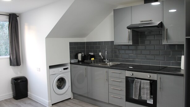 A modern kitchen with grey cabinets, a built-in oven, a washing machine, and a sink. - 6BV Apartment - Bevois Valley (Southampton)
