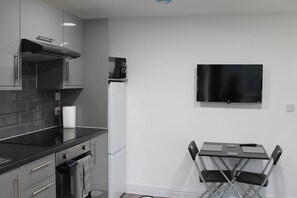 Una cocina moderna con televisor de pantalla plana, microondas y un pequeño comedor con mesa y sillas.