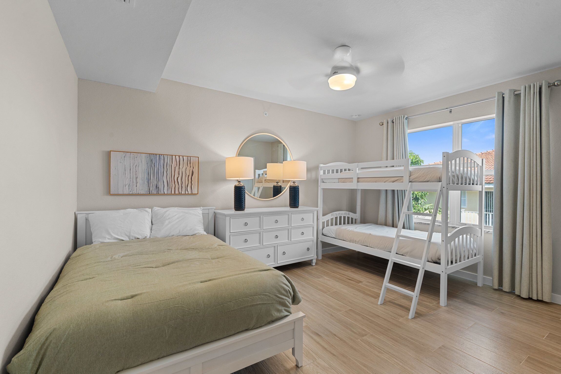 Un dormitorio con una cama litera, una cama individual, un aparador, un espejo y una ventana con cortinas.