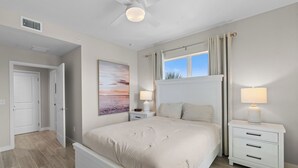 A bedroom with a bed, bedside tables, a ceiling fan, a window with curtains, and a painting on the wall. - Gulf Access with Boat Slip, Heated Saltwater Pool, Dog-Friendly - Bacino Vista #301 - Roelens (Cape Coral)