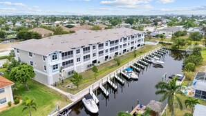 A multi-story building with a dock and boats, surrounded by greenery and residential areas. - Gulf Access with Boat Slip, Heated Saltwater Pool, Dog-Friendly - Bacino Vista #206 - Roelens (Cape Coral)