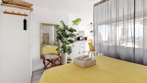Een kamer met een bed, een stoel, een spiegel, een plant en een kitchenette.