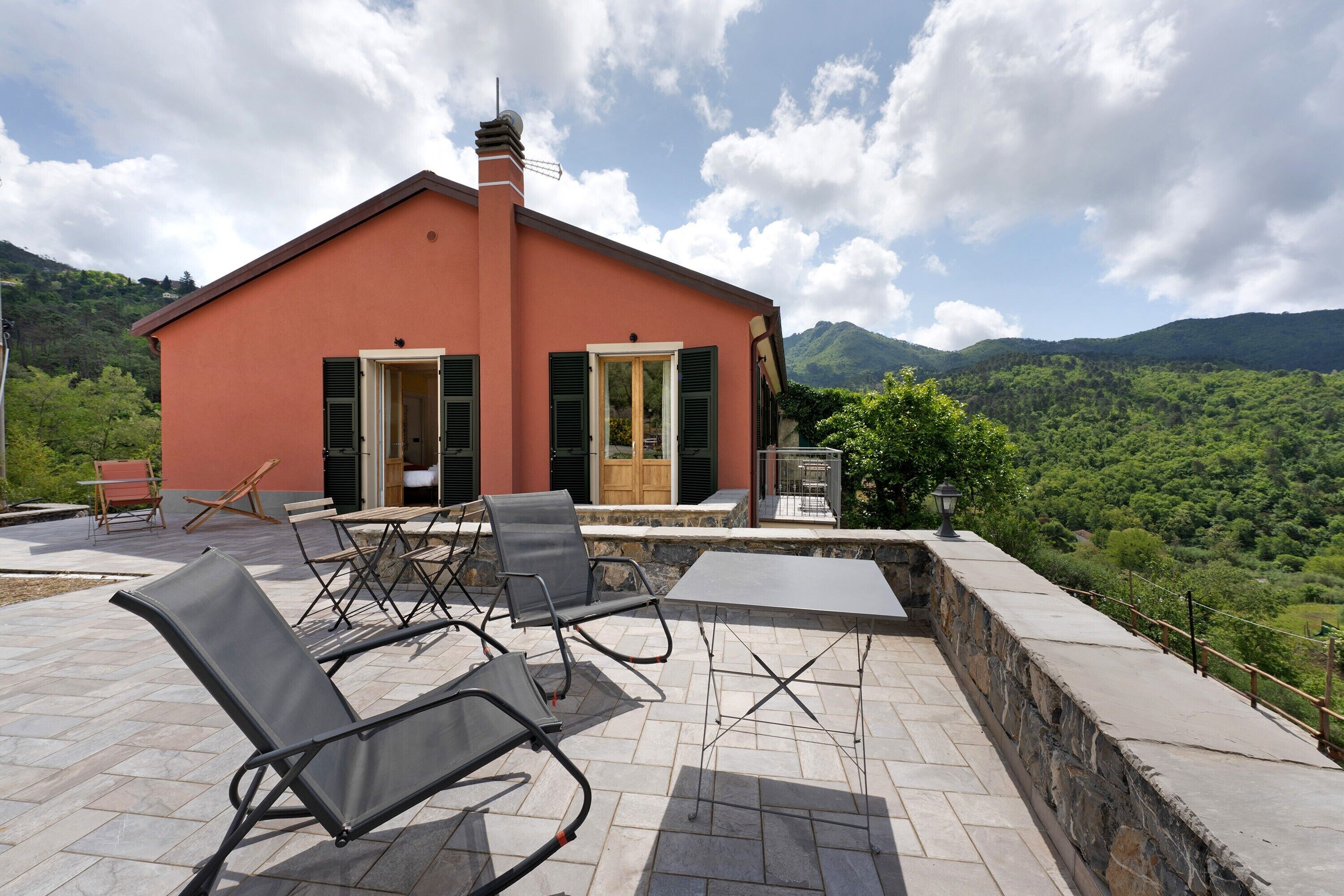 A red villa with a patio, outdoor furniture, and a view of green hills.