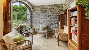 Una habitación acogedora con paredes de piedra, una estantería de madera, mobiliario de mimbre y vistas al exterior.