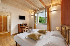 A bedroom with a bed, a desk, a TV, and a window with curtains.