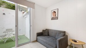 A room with a grey sofa, a small wooden table, and a sliding glass door leading to a patio with a white wall and a framed picture on the wall. - Apartment 'Lisboa Sweet For Familys' with Private Terrace, Wi-Fi and Air Conditioning (Lisboa)