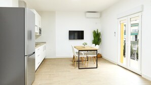 A modern kitchen with a built-in refrigerator, a dining table with chairs, a flat-screen TV mounted on the wall, and a potted plant.