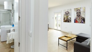 A modern hotel room with a bathroom, a dining area with a table and chairs, and artwork on the walls.